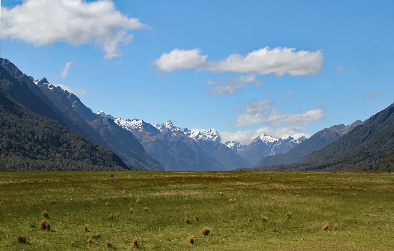 La Milford Road remontant une large vallée vers des montagnes enneigées sous un ciel bleu