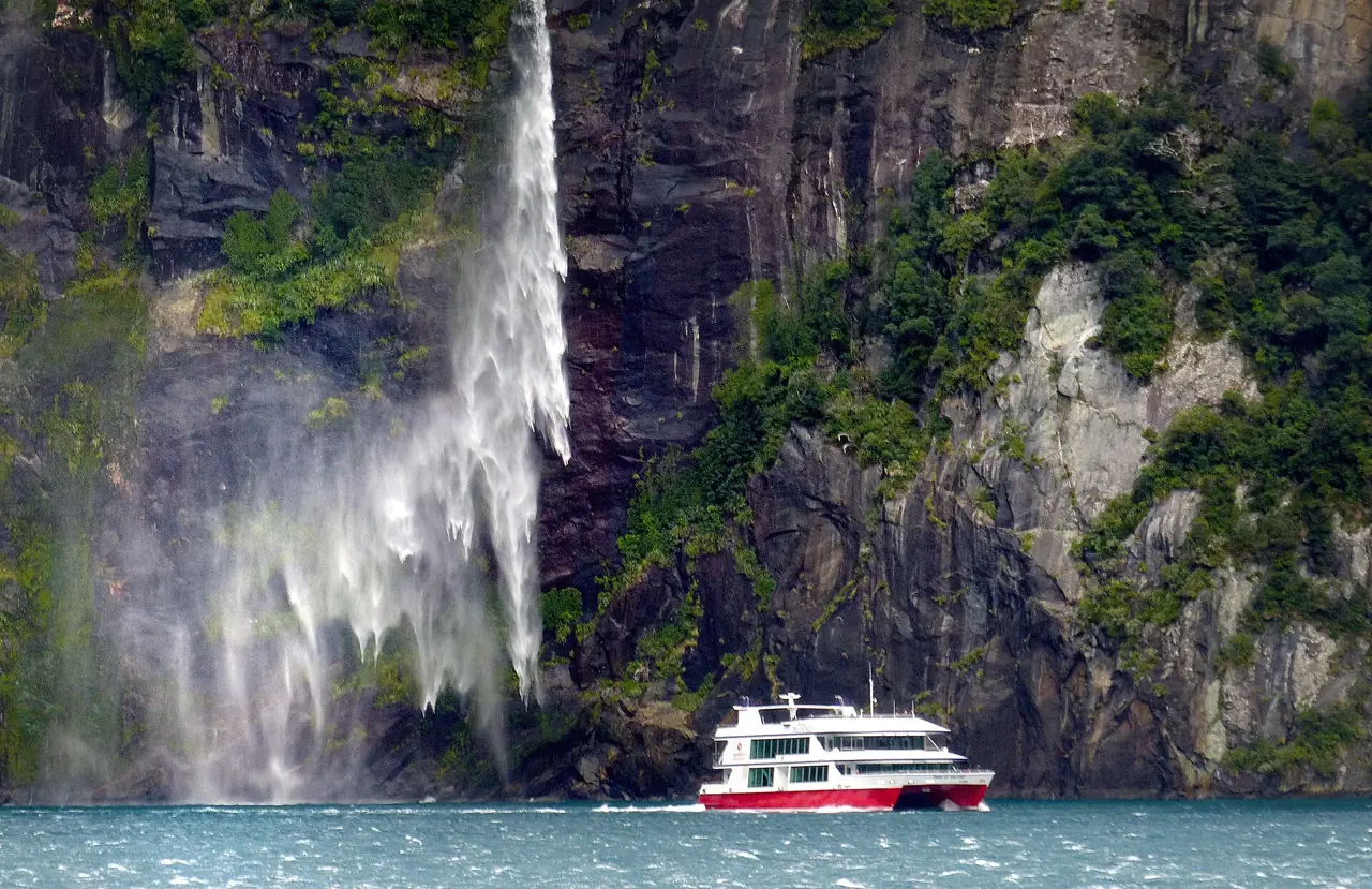 A cruise boat passing below a waterfall in Milford Sound