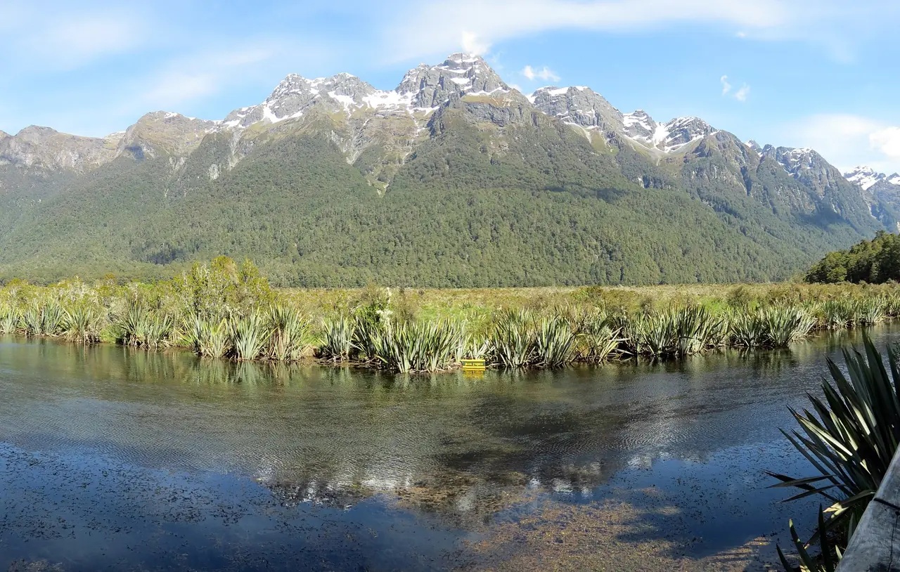 Snowy mountains reflected in a still lake beside the Milford Road