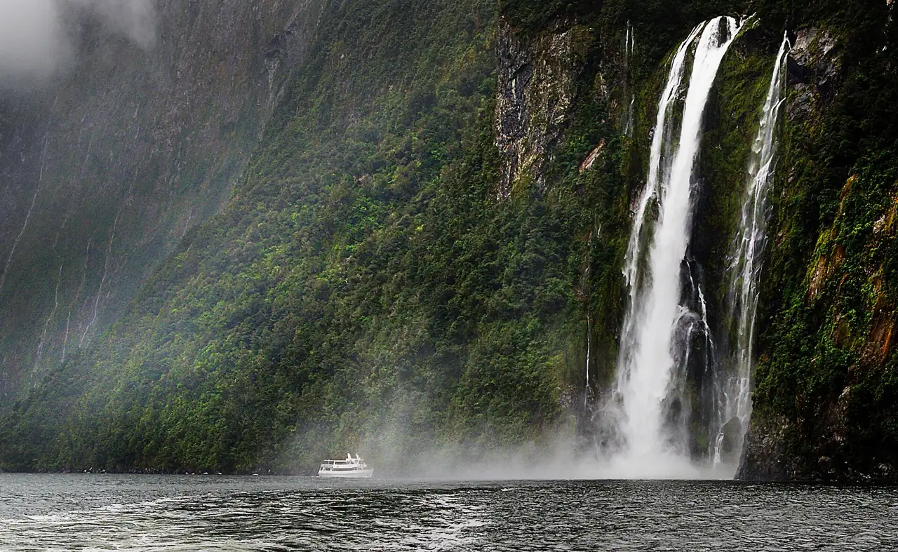 Stirling Falls dropping into the fiord, with a boat at its base